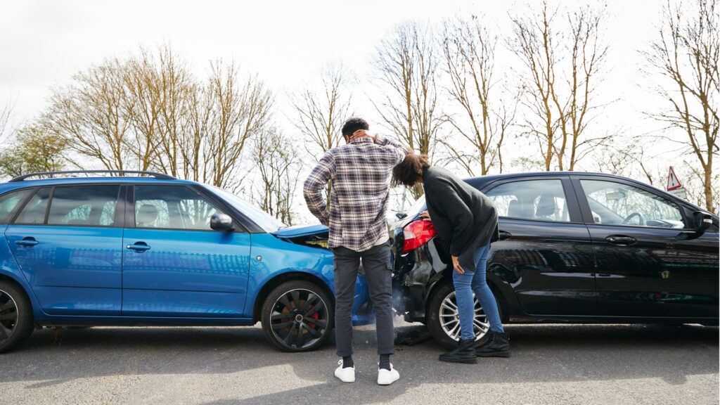 Who is at fault in a rear-end collision? Two people look at a crash site between their cars to determine rear-end collision fault.